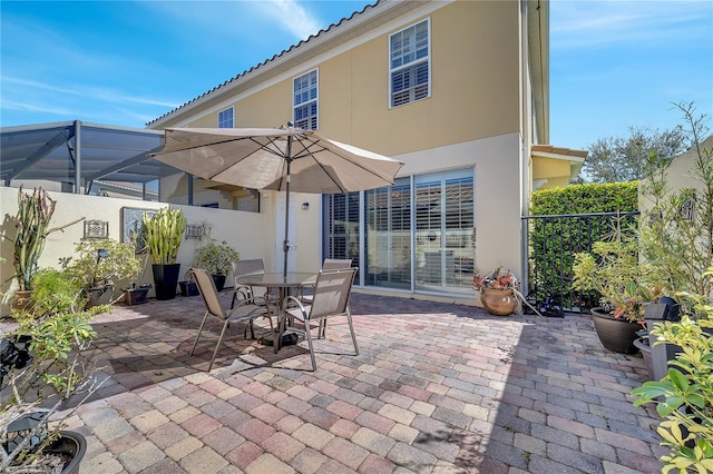 view of patio featuring glass enclosure, outdoor dining area, and a fenced backyard