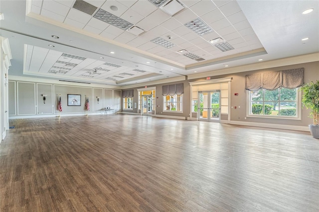 unfurnished living room with baseboards, wood finished floors, a tray ceiling, crown molding, and french doors