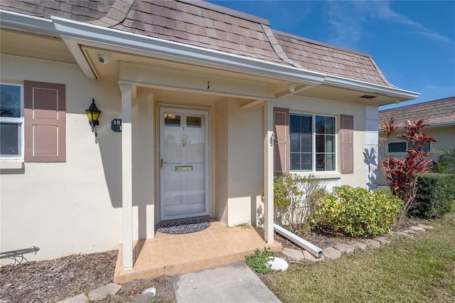 entrance to property with stucco siding, mansard roof, and roof with shingles