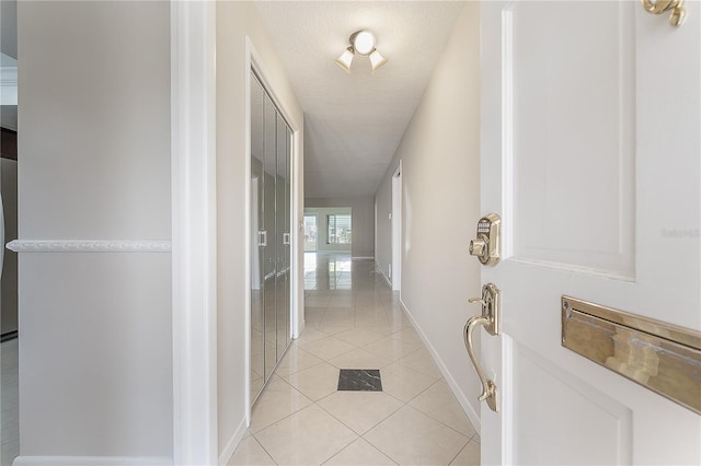 hall featuring light tile patterned flooring, a textured ceiling, and baseboards