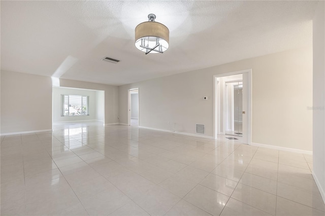 spare room featuring light tile patterned floors, a textured ceiling, visible vents, and baseboards