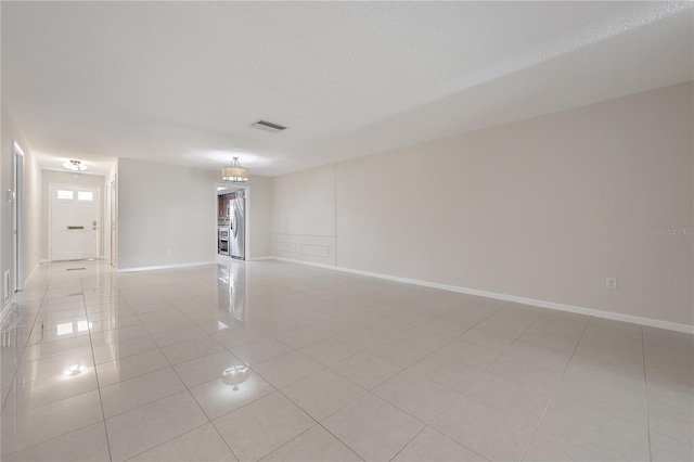 empty room with visible vents, a textured ceiling, baseboards, and light tile patterned floors