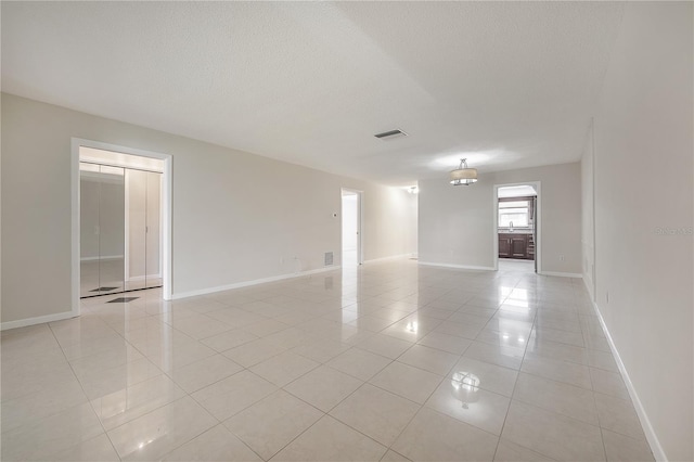 spare room with light tile patterned floors, visible vents, baseboards, and a textured ceiling