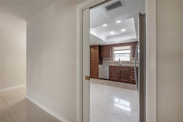 hall featuring a tray ceiling, light tile patterned floors, visible vents, ornamental molding, and baseboards