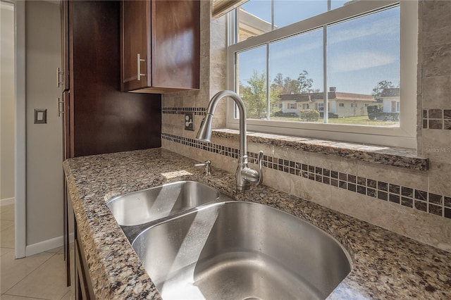 kitchen with stone counters, light tile patterned flooring, a sink, baseboards, and backsplash