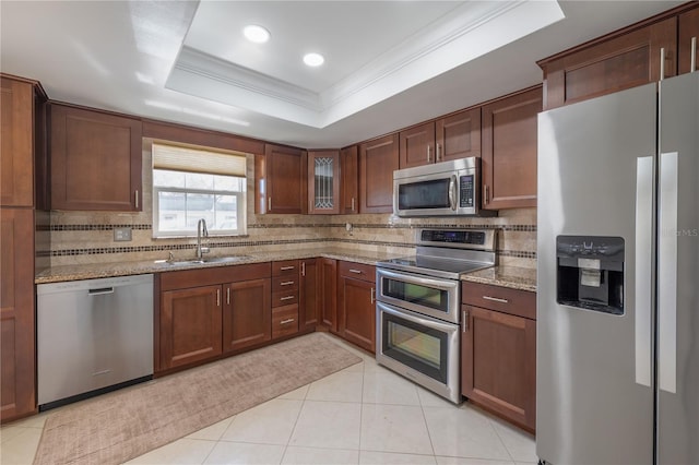 kitchen featuring ornamental molding, light stone countertops, a tray ceiling, stainless steel appliances, and a sink