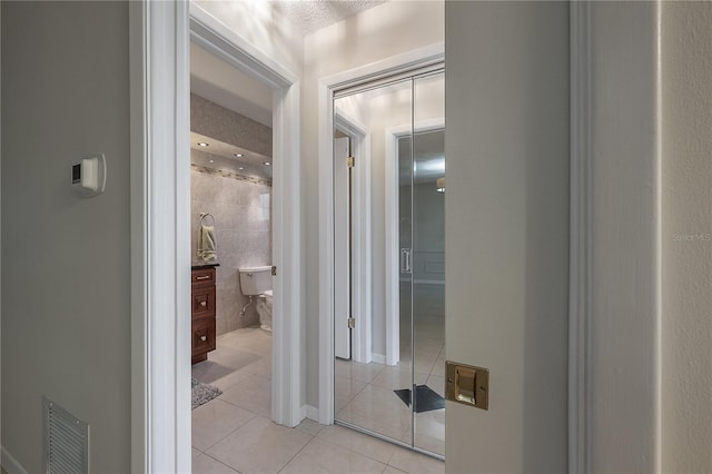 corridor featuring light tile patterned flooring, visible vents, and tile walls