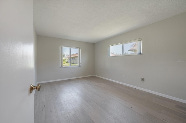 empty room featuring a textured ceiling, plenty of natural light, wood finished floors, and baseboards