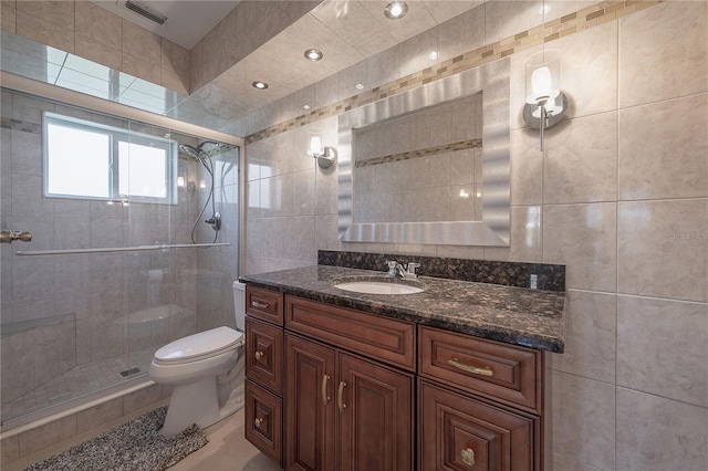 bathroom with tile walls, visible vents, toilet, a shower stall, and vanity