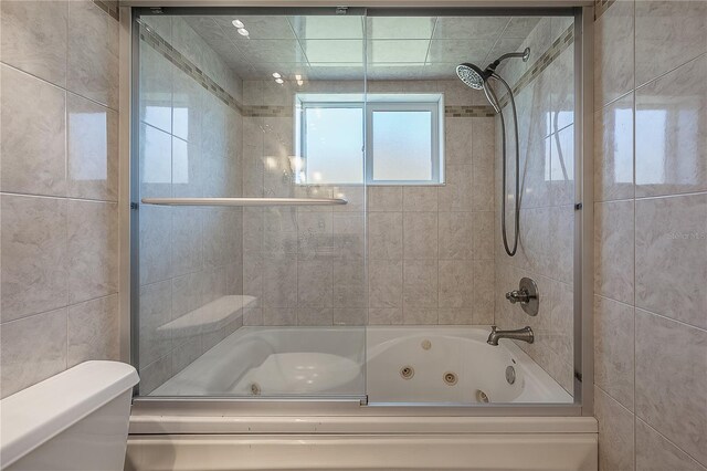 bathroom featuring a combined bath / shower with jetted tub, toilet, and tile walls