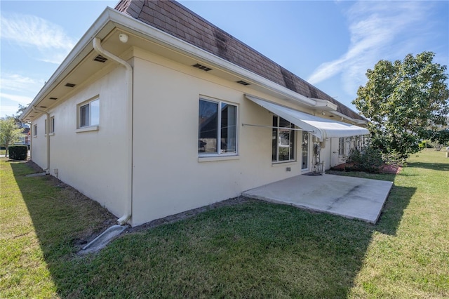 back of property featuring roof with shingles, a patio, stucco siding, mansard roof, and a lawn