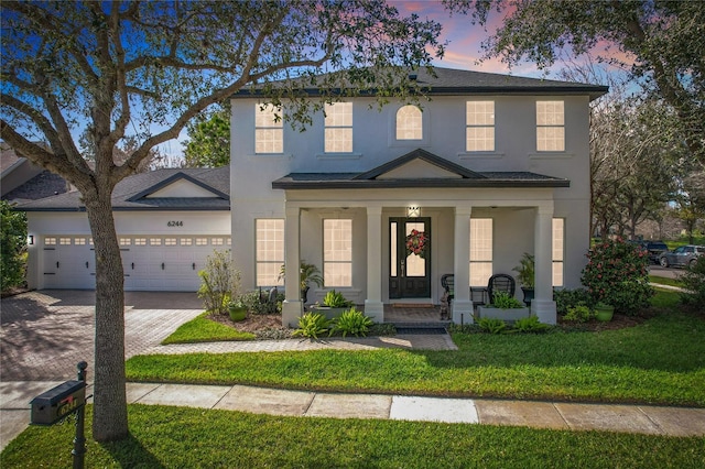 view of front facade with stucco siding, driveway, a porch, a front yard, and an attached garage