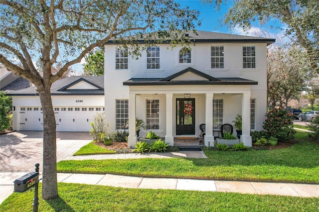 view of front of house featuring stucco siding, an attached garage, covered porch, and driveway