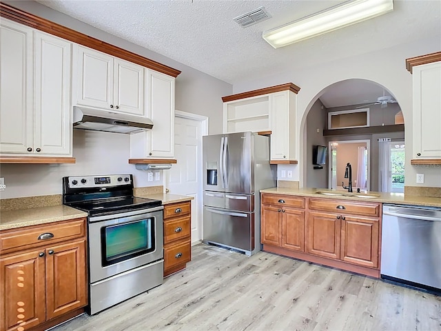 kitchen featuring arched walkways, under cabinet range hood, a sink, visible vents, and appliances with stainless steel finishes