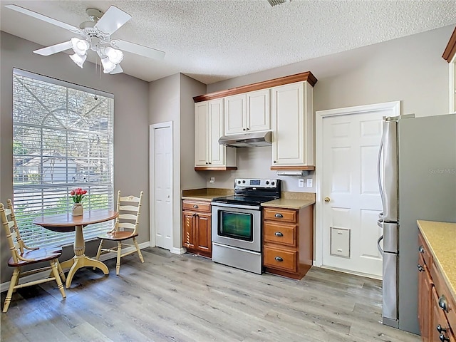 kitchen featuring light countertops, appliances with stainless steel finishes, a textured ceiling, light wood-type flooring, and under cabinet range hood