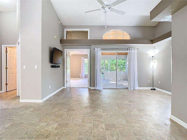 interior space with ceiling fan, a towering ceiling, and baseboards