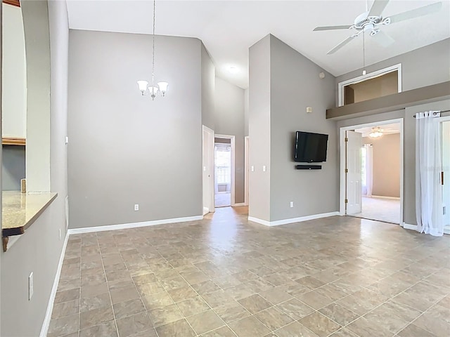 unfurnished living room with ceiling fan with notable chandelier, high vaulted ceiling, and baseboards