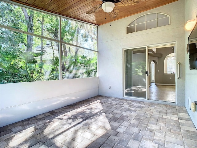 unfurnished sunroom with a ceiling fan, arched walkways, wood ceiling, and a healthy amount of sunlight