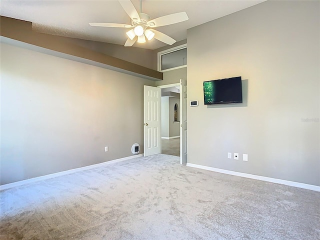 carpeted empty room featuring lofted ceiling, arched walkways, a ceiling fan, and baseboards