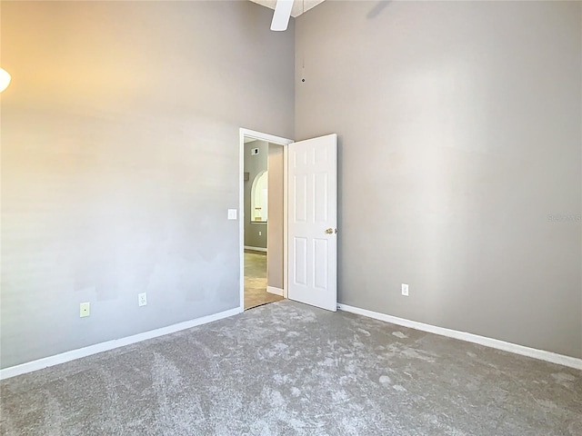 spare room featuring arched walkways, a high ceiling, baseboards, and unfinished concrete floors