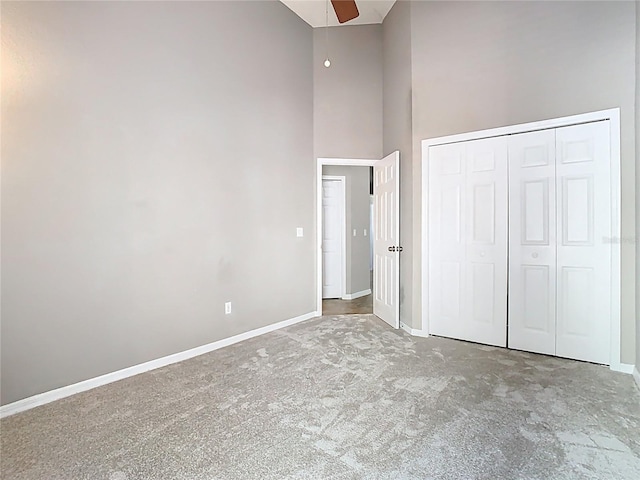 unfurnished bedroom with baseboards, a towering ceiling, ceiling fan, carpet, and a closet