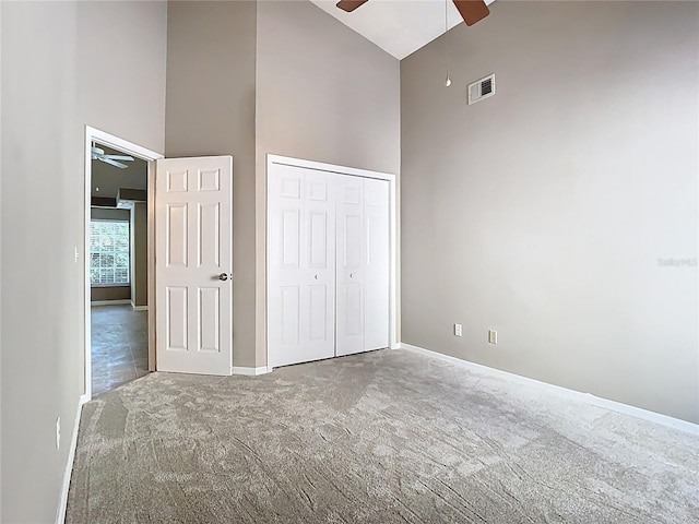 unfurnished bedroom with a closet, visible vents, a towering ceiling, carpet flooring, and baseboards