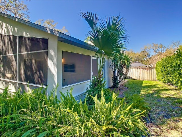 view of side of property featuring fence, a lawn, and stucco siding