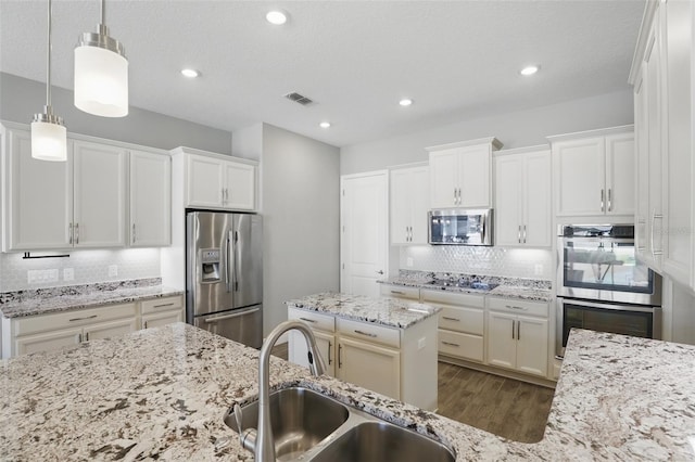 kitchen featuring visible vents, dark wood finished floors, a sink, decorative backsplash, and stainless steel appliances