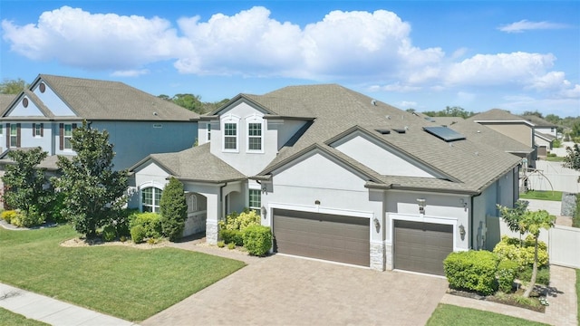 view of front of home with a front yard, stucco siding, driveway, stone siding, and an attached garage