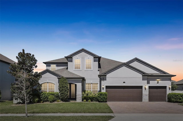 view of front of home featuring stucco siding, decorative driveway, roof with shingles, an attached garage, and a front yard