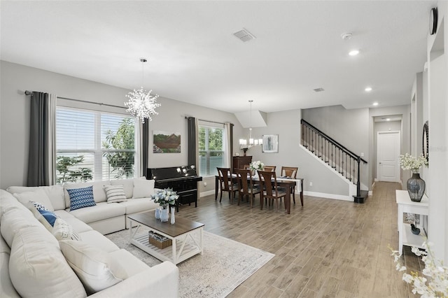 living area featuring a chandelier, visible vents, light wood finished floors, and stairs