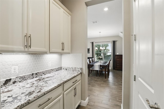 kitchen with light stone countertops, visible vents, light wood finished floors, decorative backsplash, and a chandelier