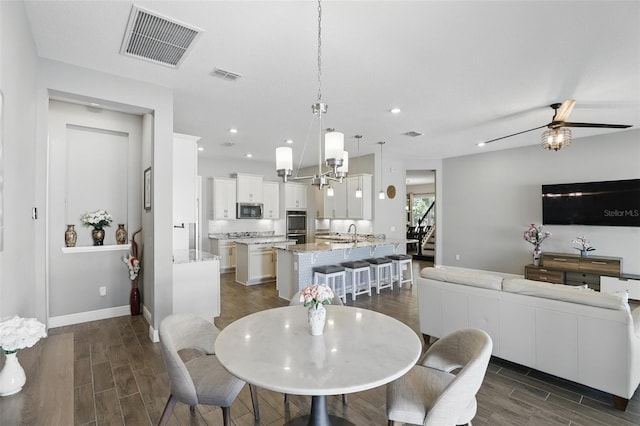 dining area with stairs, visible vents, wood tiled floor, and ceiling fan with notable chandelier