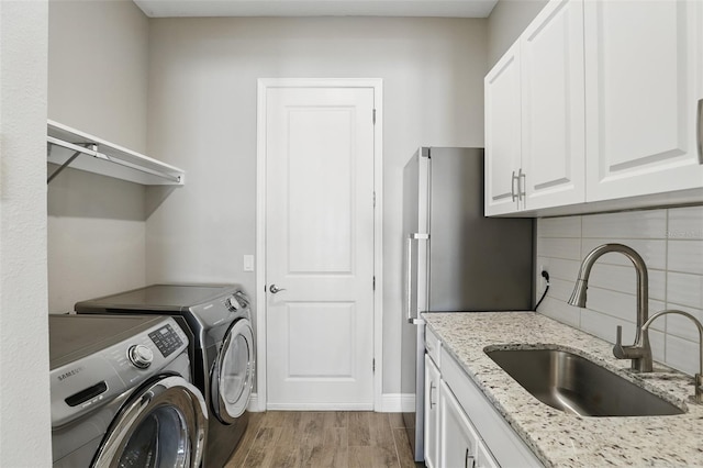 laundry area featuring baseboards, light wood-type flooring, washer and dryer, cabinet space, and a sink