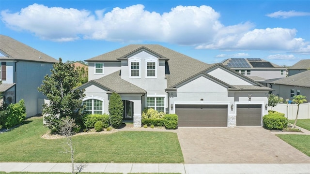 traditional-style house featuring fence, an attached garage, stucco siding, a front lawn, and decorative driveway