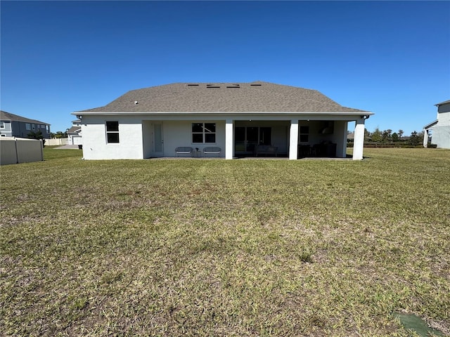 rear view of property featuring a shingled roof, a lawn, and stucco siding