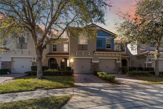 view of front of house with an attached garage, stone siding, decorative driveway, and stucco siding