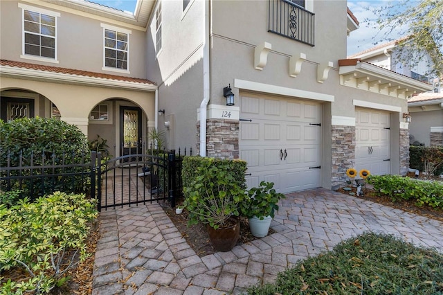 exterior space with stone siding, an attached garage, a gate, fence, and stucco siding