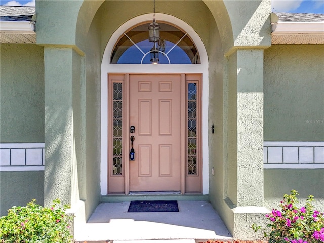 property entrance with roof with shingles and stucco siding