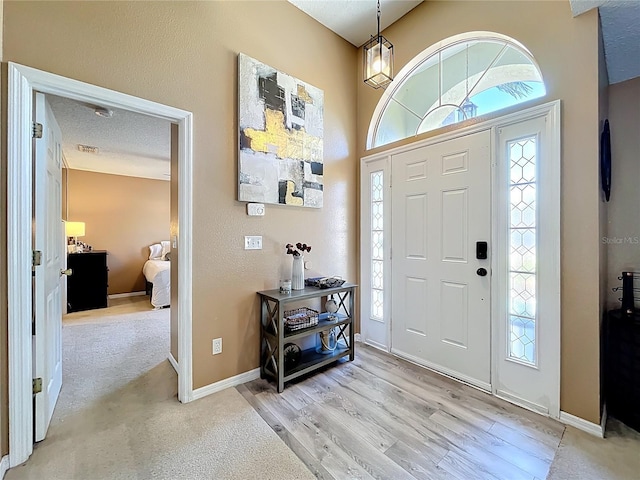 foyer entrance featuring light wood-style floors, visible vents, a textured ceiling, and baseboards