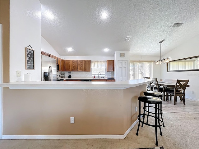 kitchen with lofted ceiling, visible vents, brown cabinets, and stainless steel fridge with ice dispenser