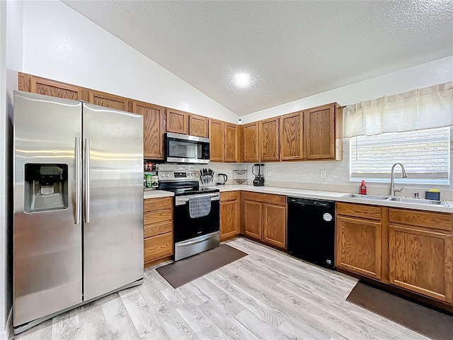 kitchen featuring appliances with stainless steel finishes, brown cabinets, vaulted ceiling, light countertops, and a sink