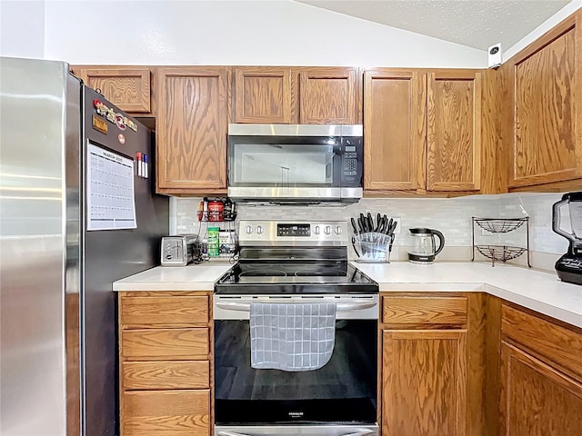 kitchen with tasteful backsplash, brown cabinetry, vaulted ceiling, stainless steel appliances, and light countertops