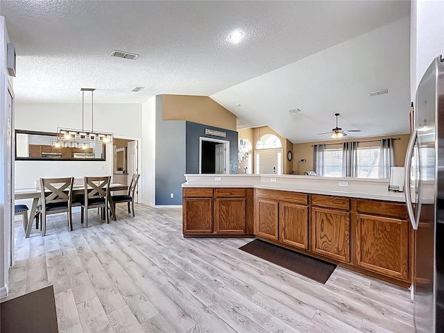 kitchen featuring visible vents, brown cabinetry, lofted ceiling, stainless steel refrigerator, and light countertops