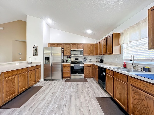 kitchen with a sink, vaulted ceiling, appliances with stainless steel finishes, brown cabinets, and light wood finished floors