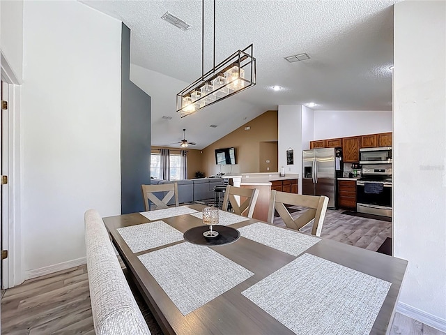 dining space with visible vents, a ceiling fan, lofted ceiling, a textured ceiling, and light wood-style floors