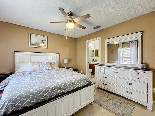 bedroom with light colored carpet, visible vents, a ceiling fan, a textured ceiling, and ensuite bath