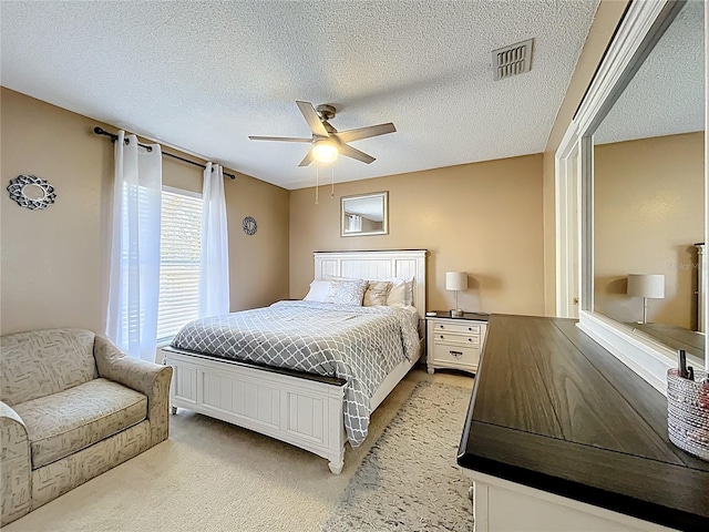 bedroom featuring light carpet, a textured ceiling, visible vents, and a ceiling fan