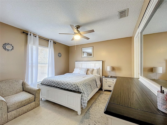 bedroom featuring ceiling fan, a textured ceiling, visible vents, and light colored carpet