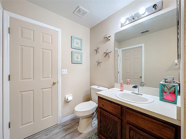 half bathroom featuring toilet, visible vents, a textured ceiling, and vanity